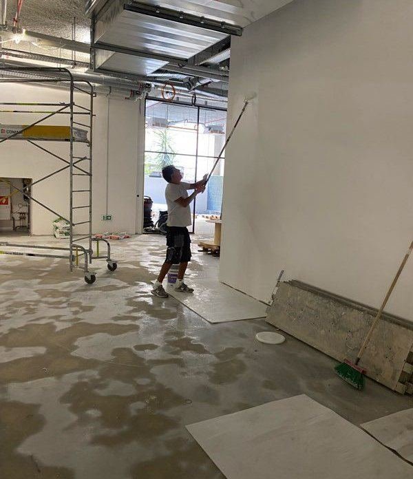 Peintre au rouleau dans un local en travaux, échafaudage roulant au fond